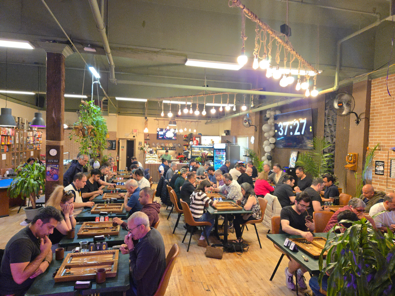 Players at long rows of tables playing backgammon during a tournament at Mench Cafe